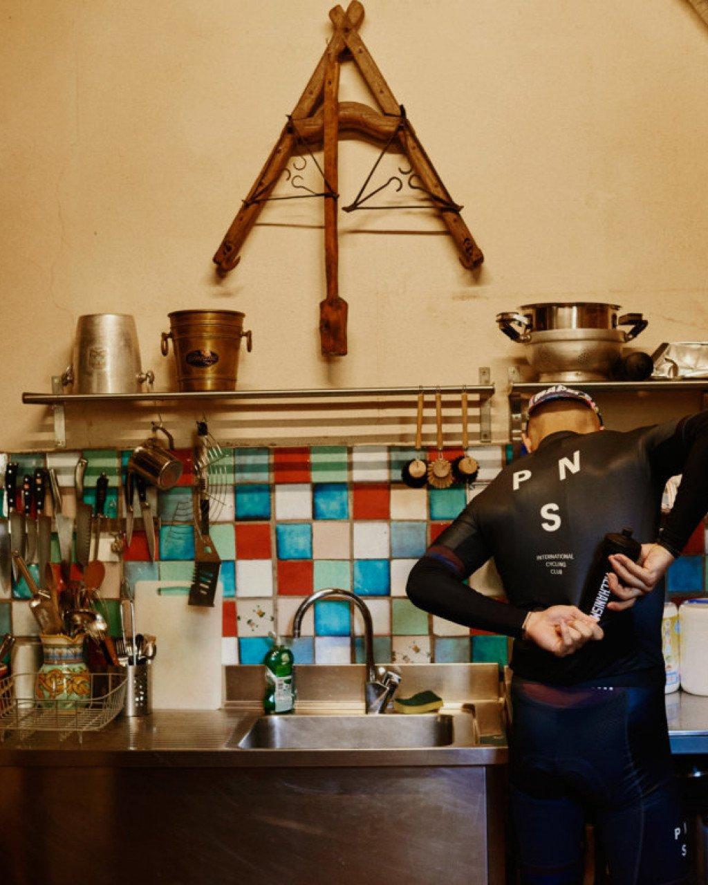Model wearing dark long-sleeve jersey with chest lettering in kitchen setting