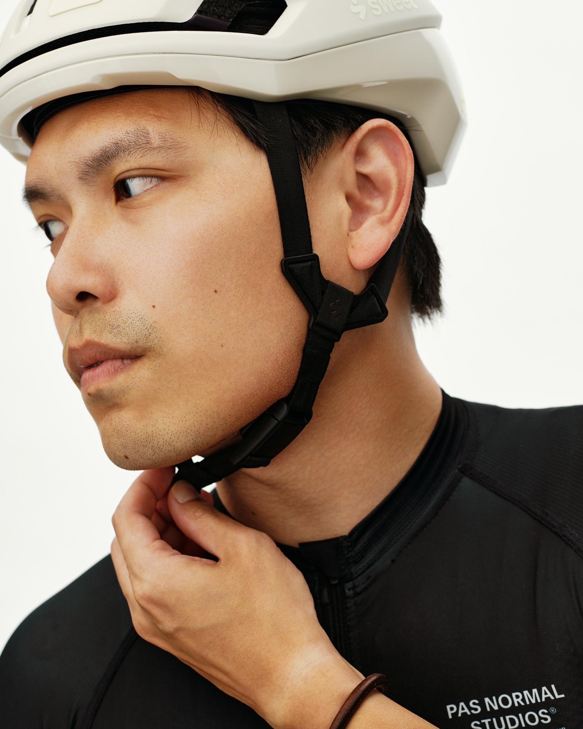 Off White Sweet Protection Falconer Aero 2Vi MIPS Round Fit cycling helmet on model, side view with chin strap being fastened