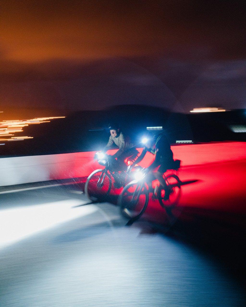 Model wearing light-colored cycling apparel riding at night with bright lights and motion blur