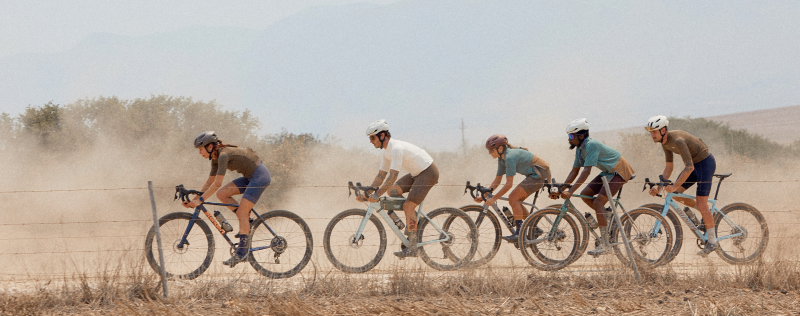 Group of cyclists racing on dusty gravel road wearing various cycling apparel