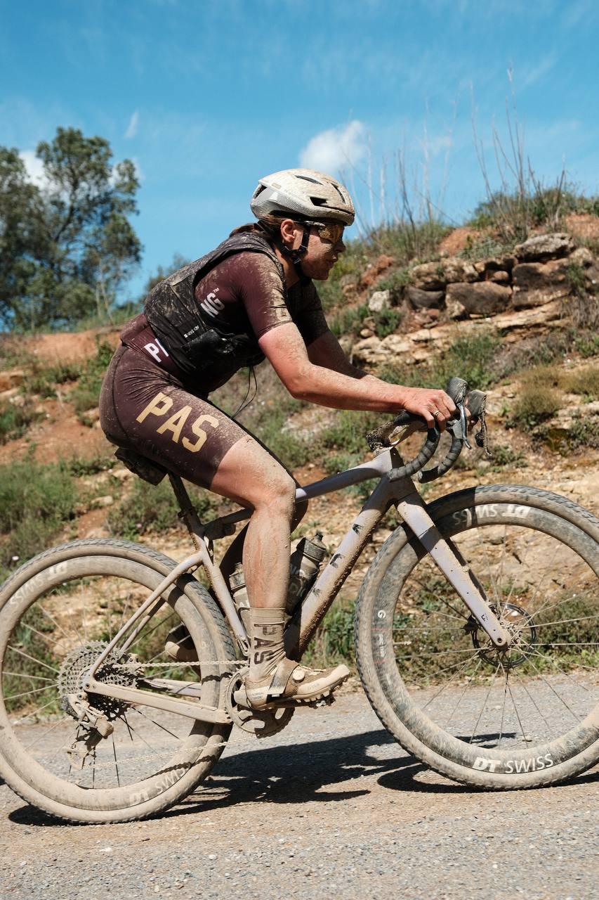 Model wearing maroon cycling kit with collection branding on gravel bike in desert terrain