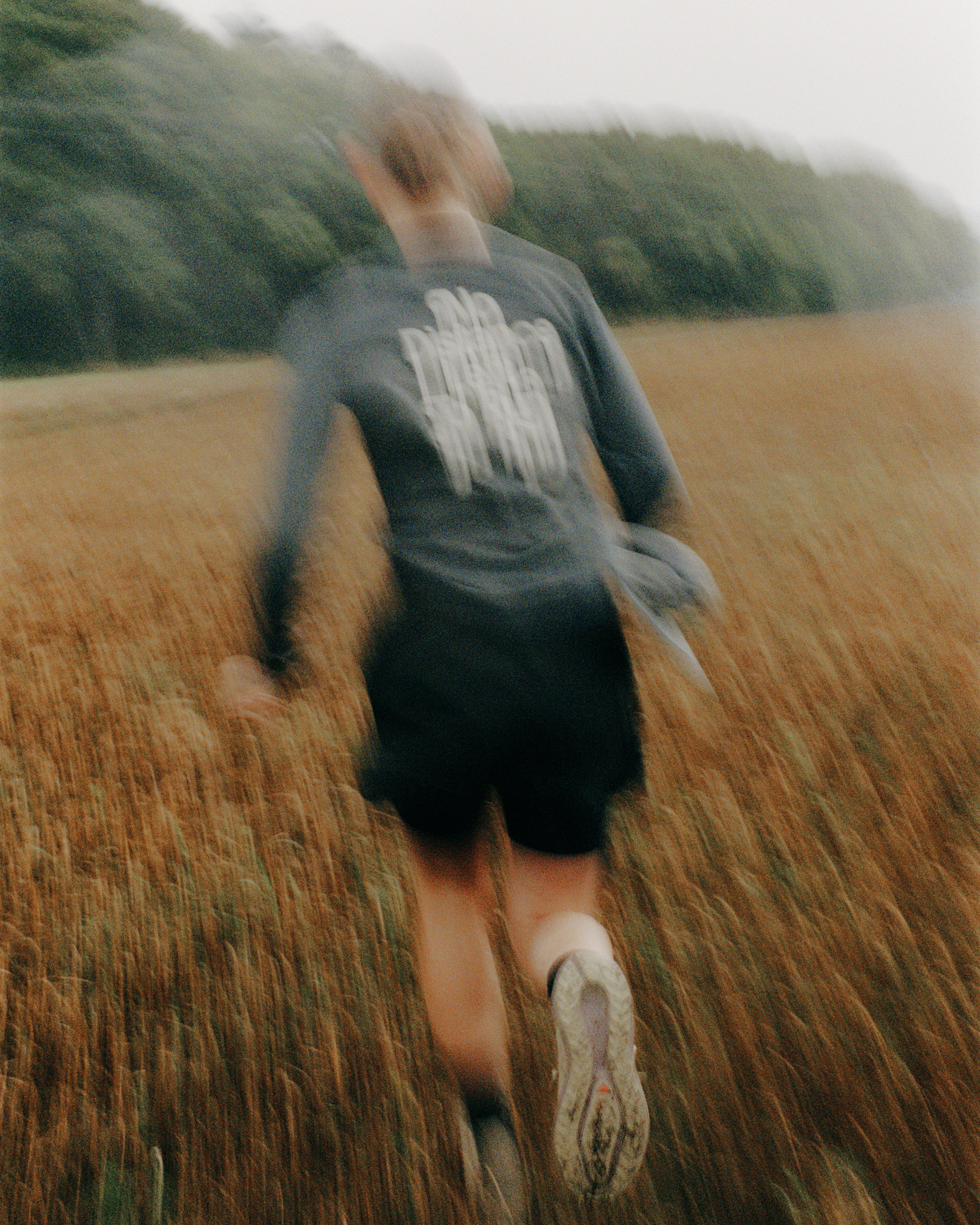 Model wearing Balance collection grey long sleeve top with white back graphic, running through field
