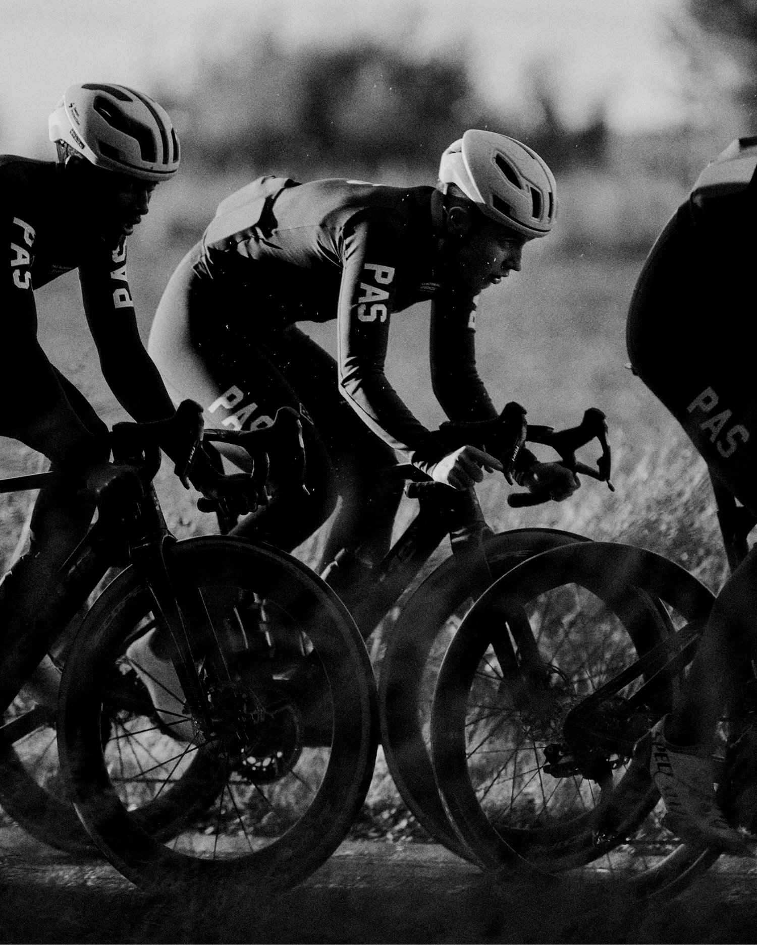 Cyclists wearing PAS collection racing gear in aerodynamic position on time trial bikes, black and white photography