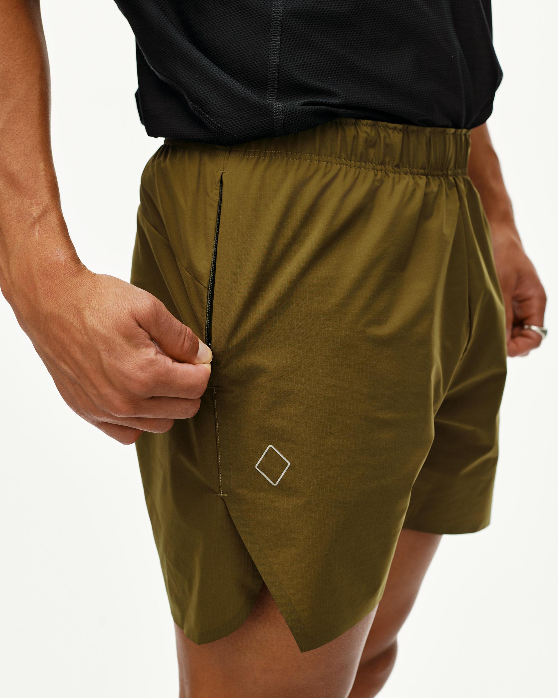 Moss Brown Balance shorts on model, side detail view with zip pocket and diamond logo