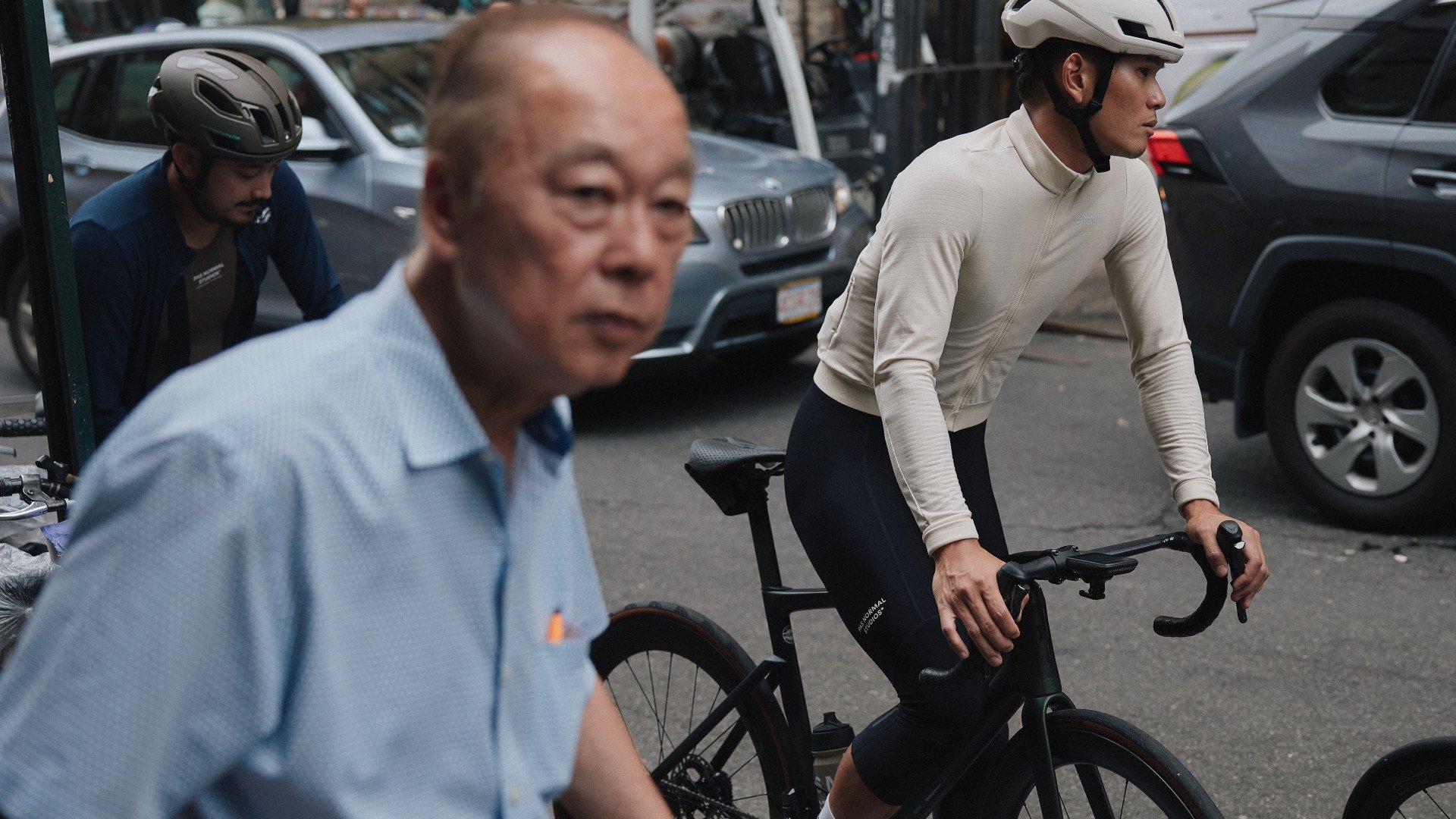 Model wearing beige long-sleeve jersey and dark bib shorts with helmet on urban street