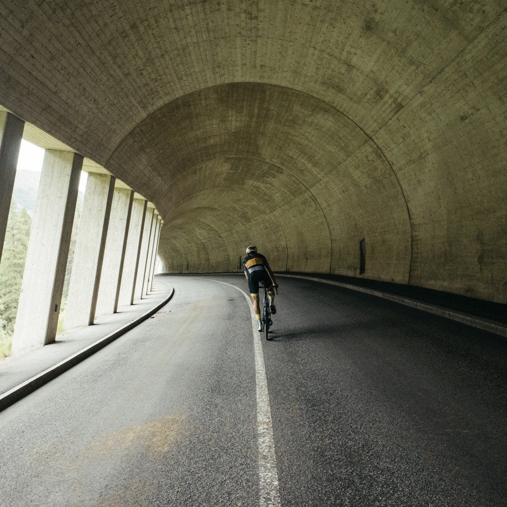Cyclist riding through concrete tunnel on curved road