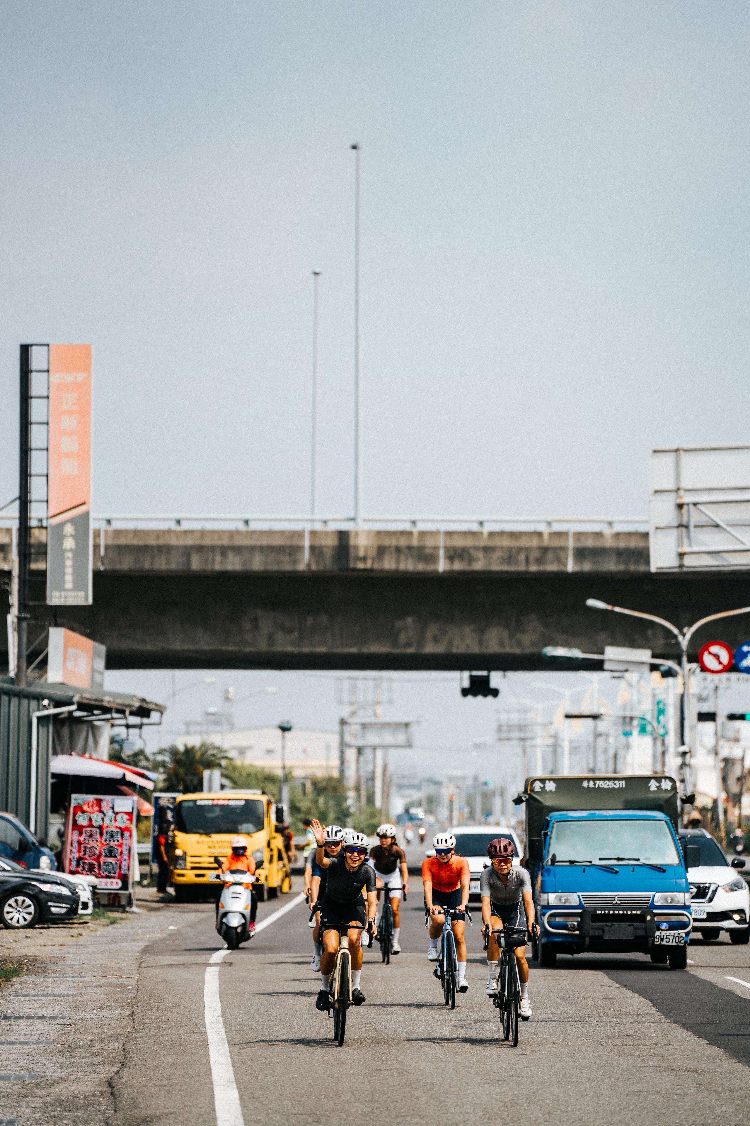 Group of cyclists riding on urban street with bridge and traffic in background