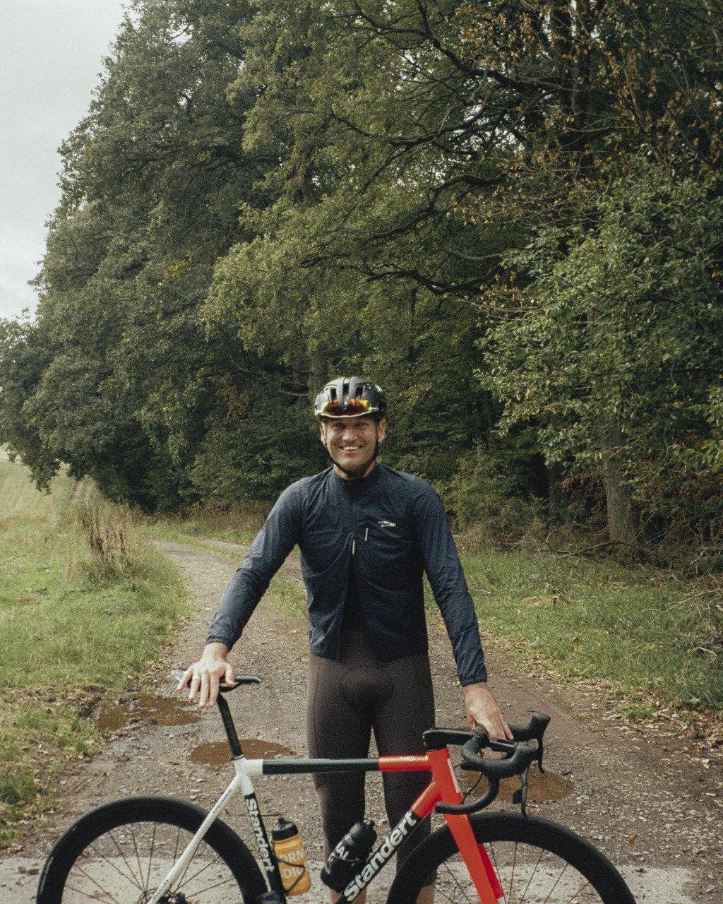 Model wearing navy Essential Long Sleeve Jersey with chest pocket, standing with bike on tree-lined path