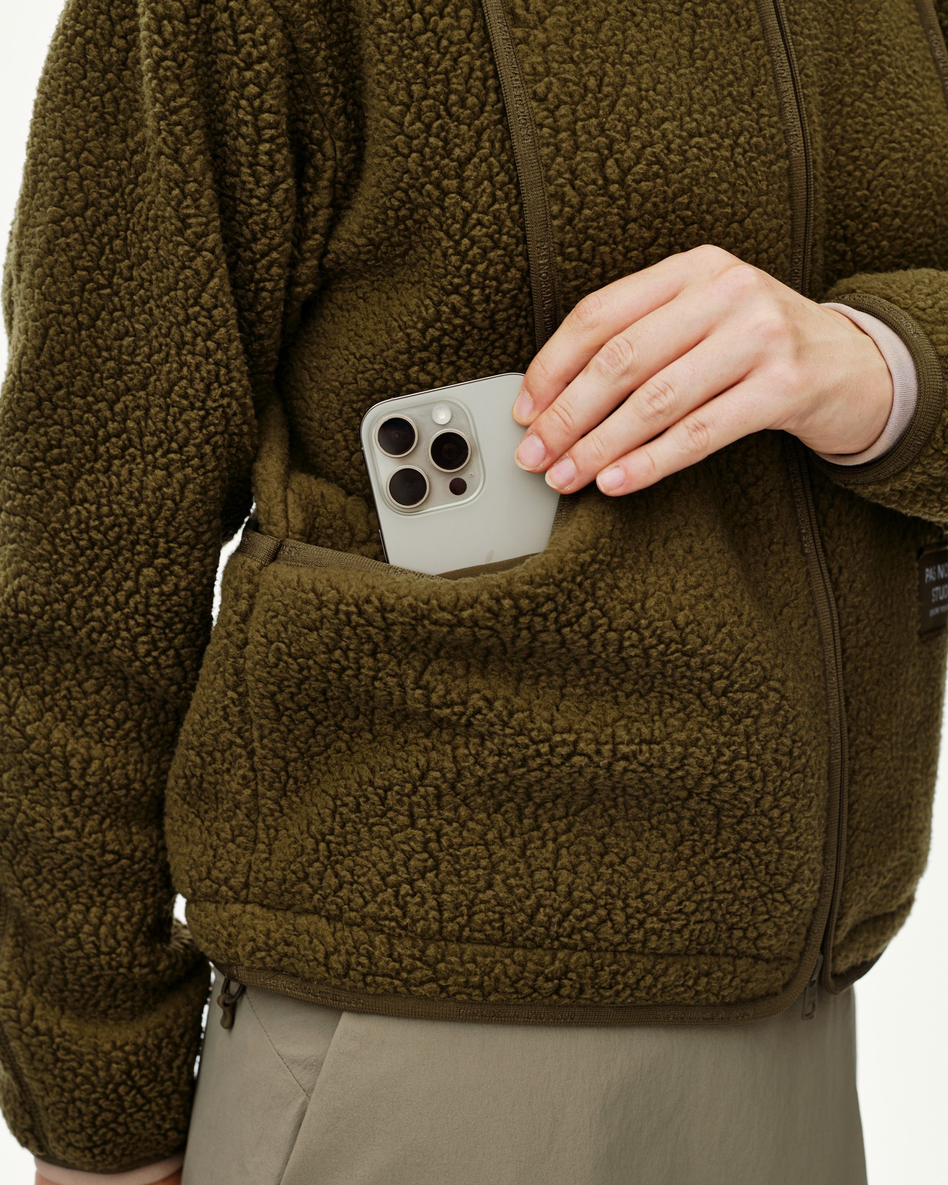 Deep Olive Off-Race Pile Fleece jacket on model, detail view of front pocket with phone being placed inside