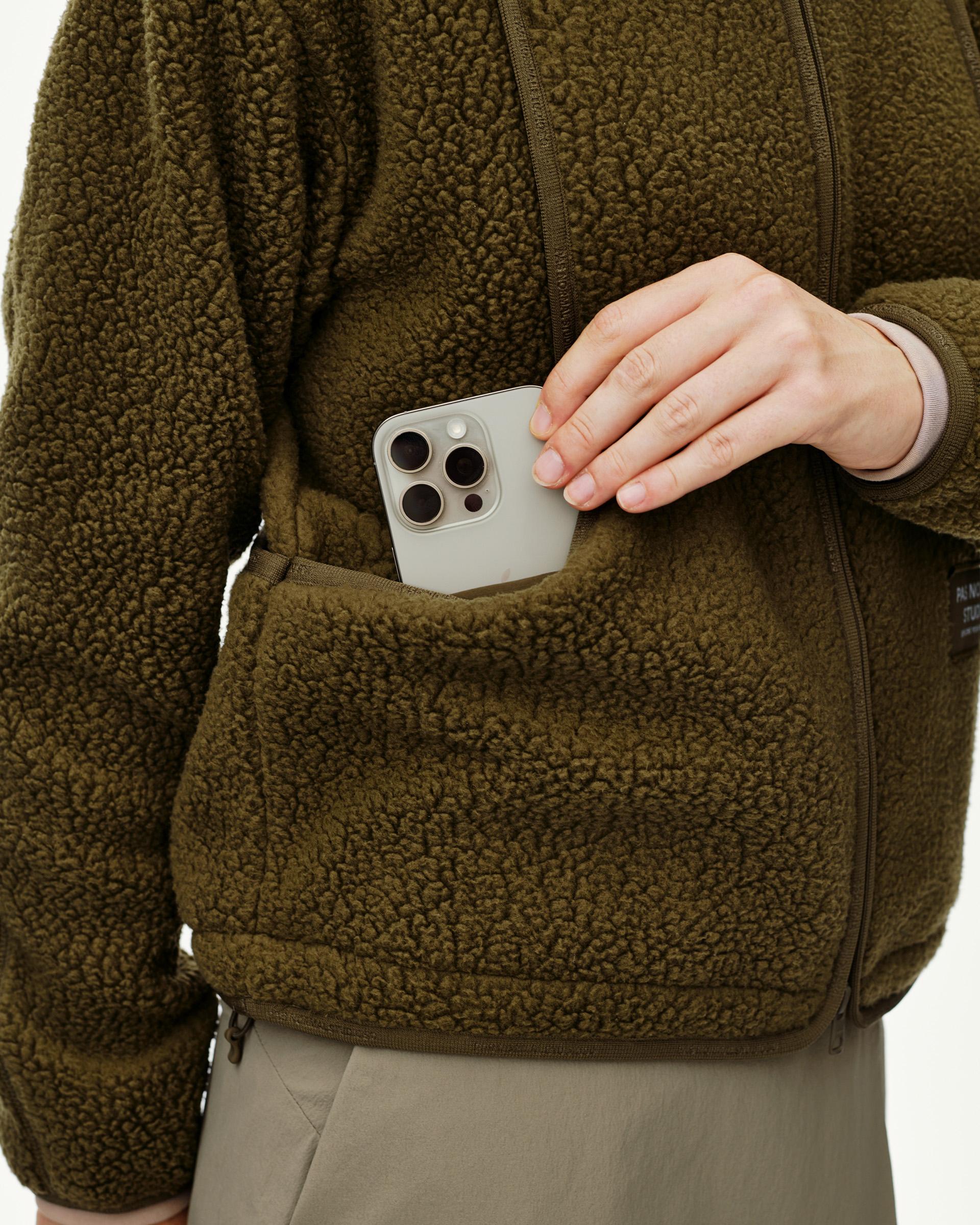 Deep Olive Off-Race Pile Fleece jacket on model, detail view of front pocket with phone being placed inside