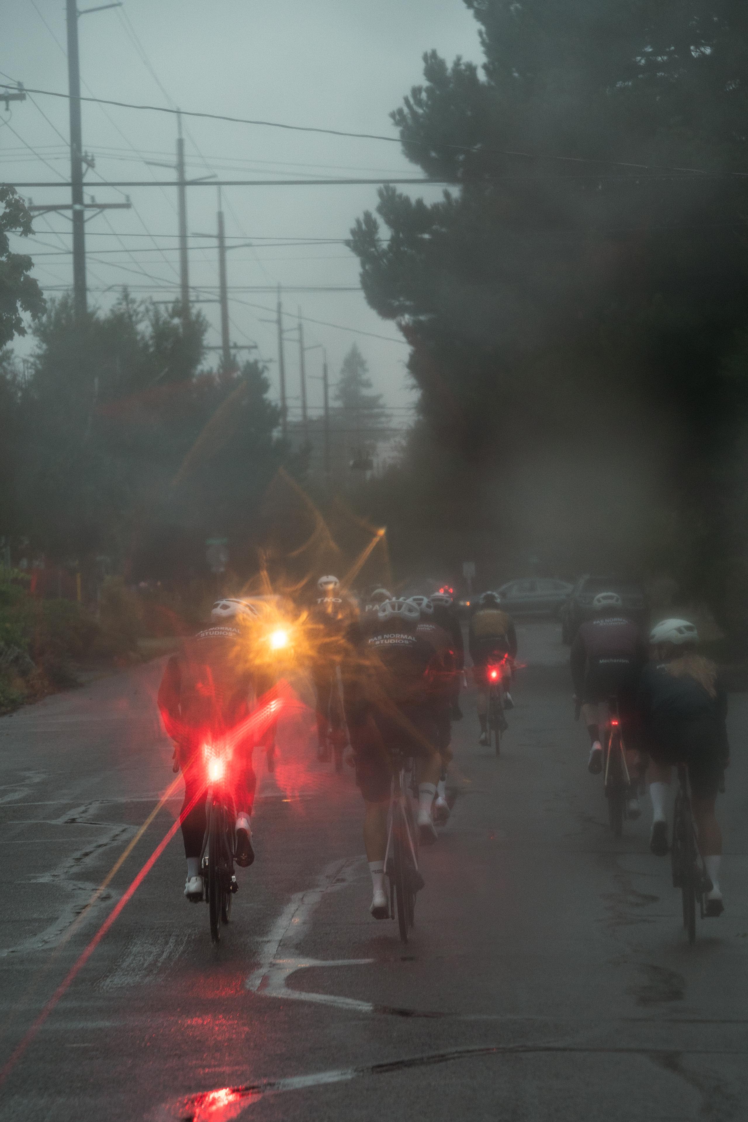 Cyclists with lights riding on wet road in foggy conditions with power lines overhead