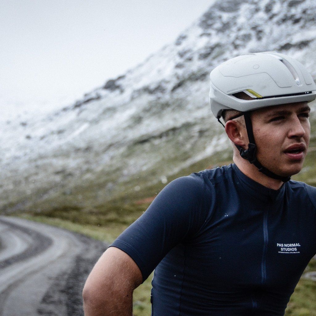 Model wearing navy cycling jersey with chest lettering and white aerodynamic helmet on mountain road
