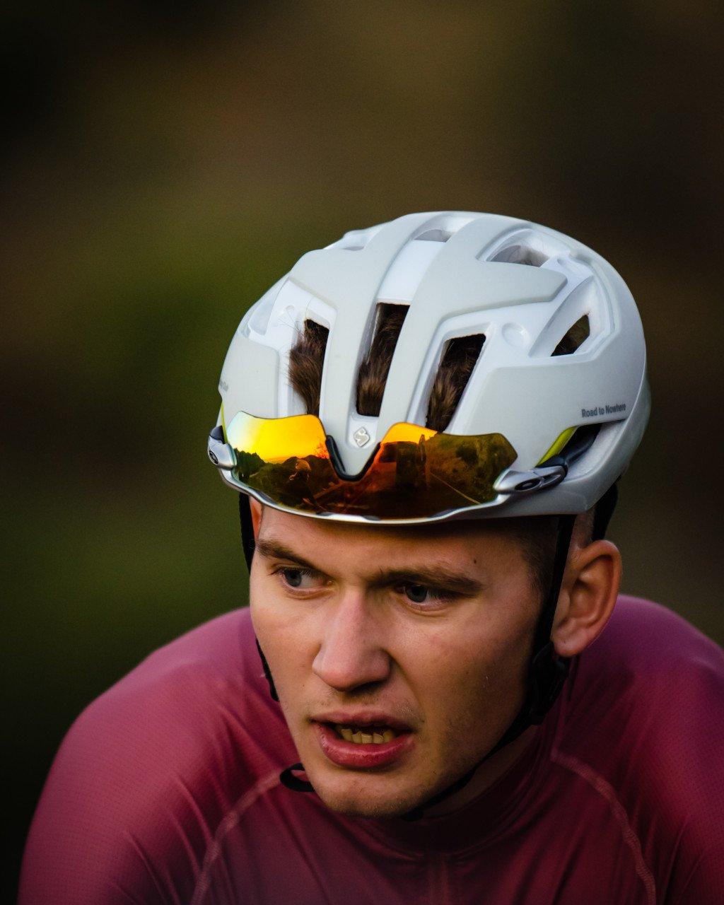 Model wearing white cycling helmet with reflective visor and purple jersey during golden hour