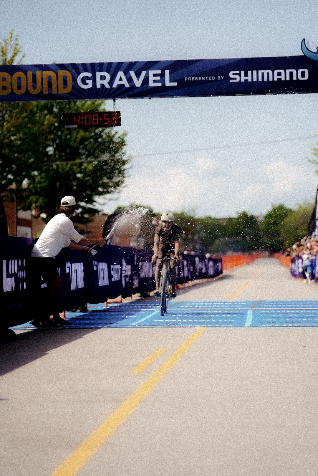 Cyclist crossing finish line at Unbound Gravel race with water spray celebration