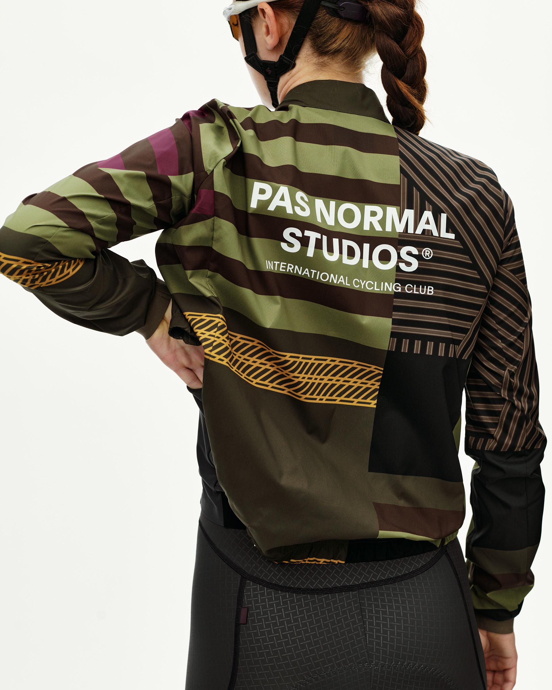 International Green Mechanism Stow Away cycling jacket on model, rear view with multicolor stripe AOP print and white logo