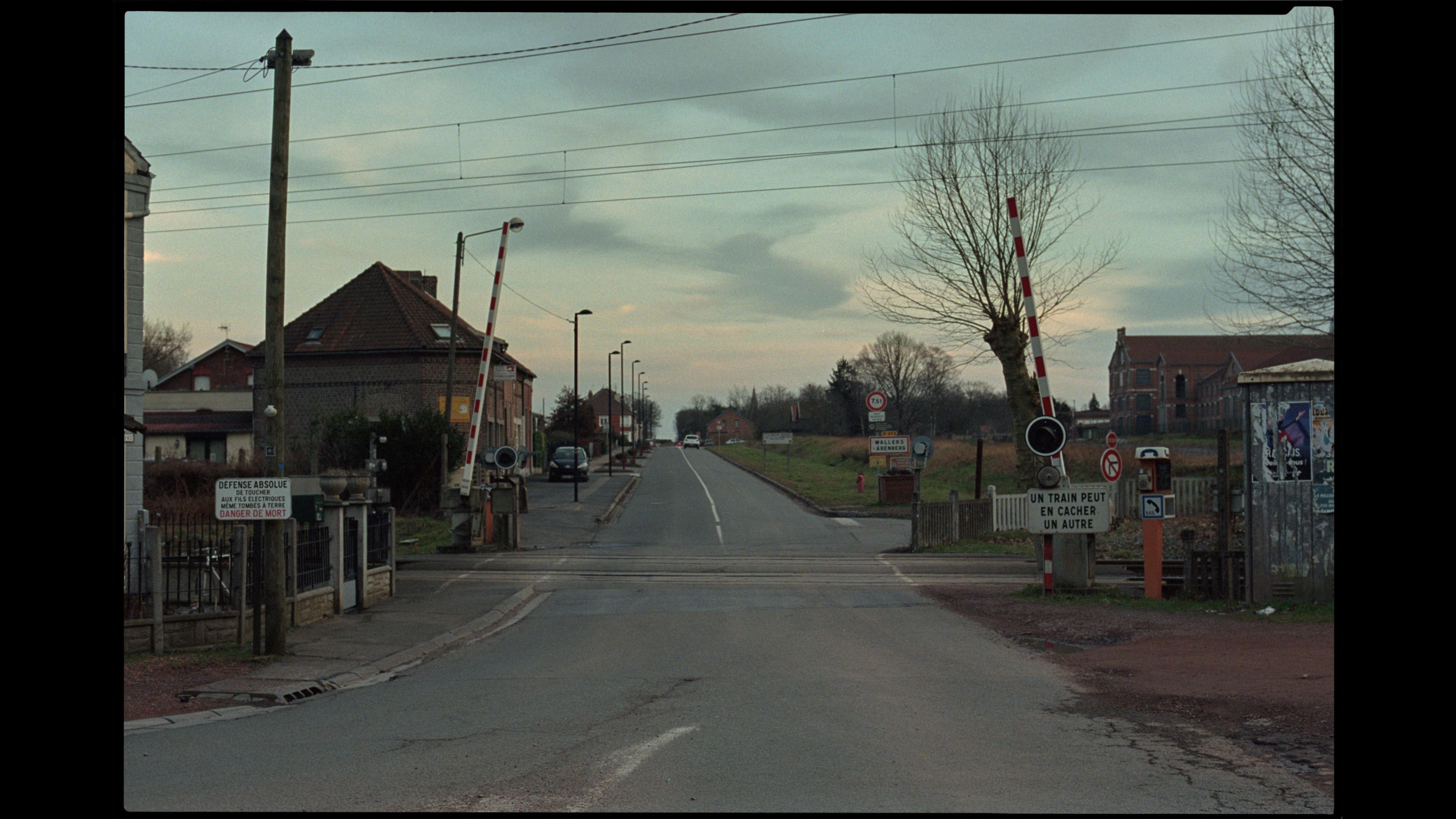 Rural Belgian street scene with railway crossing and traditional houses under overcast sky