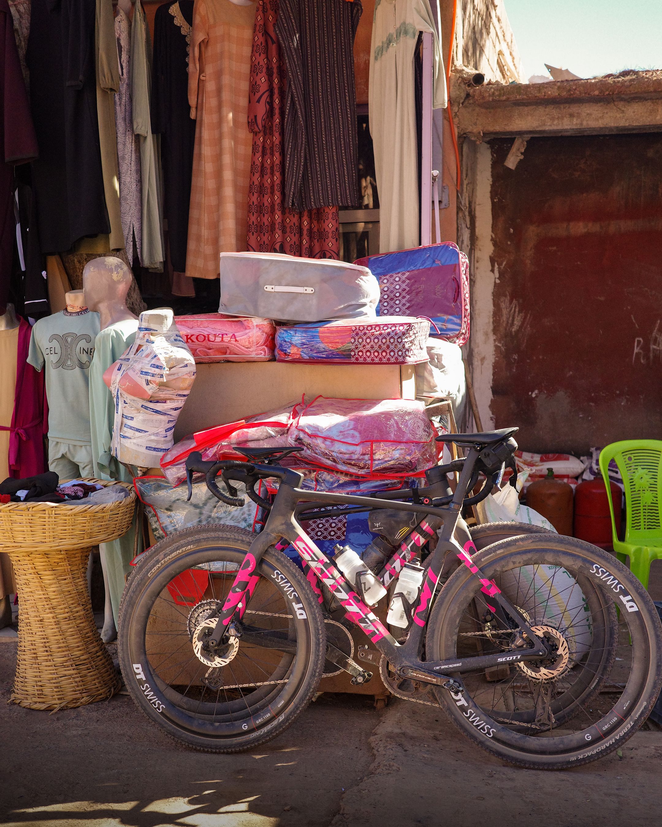 Pink and white gravel bike parked outside Moroccan market stall with textiles and baskets