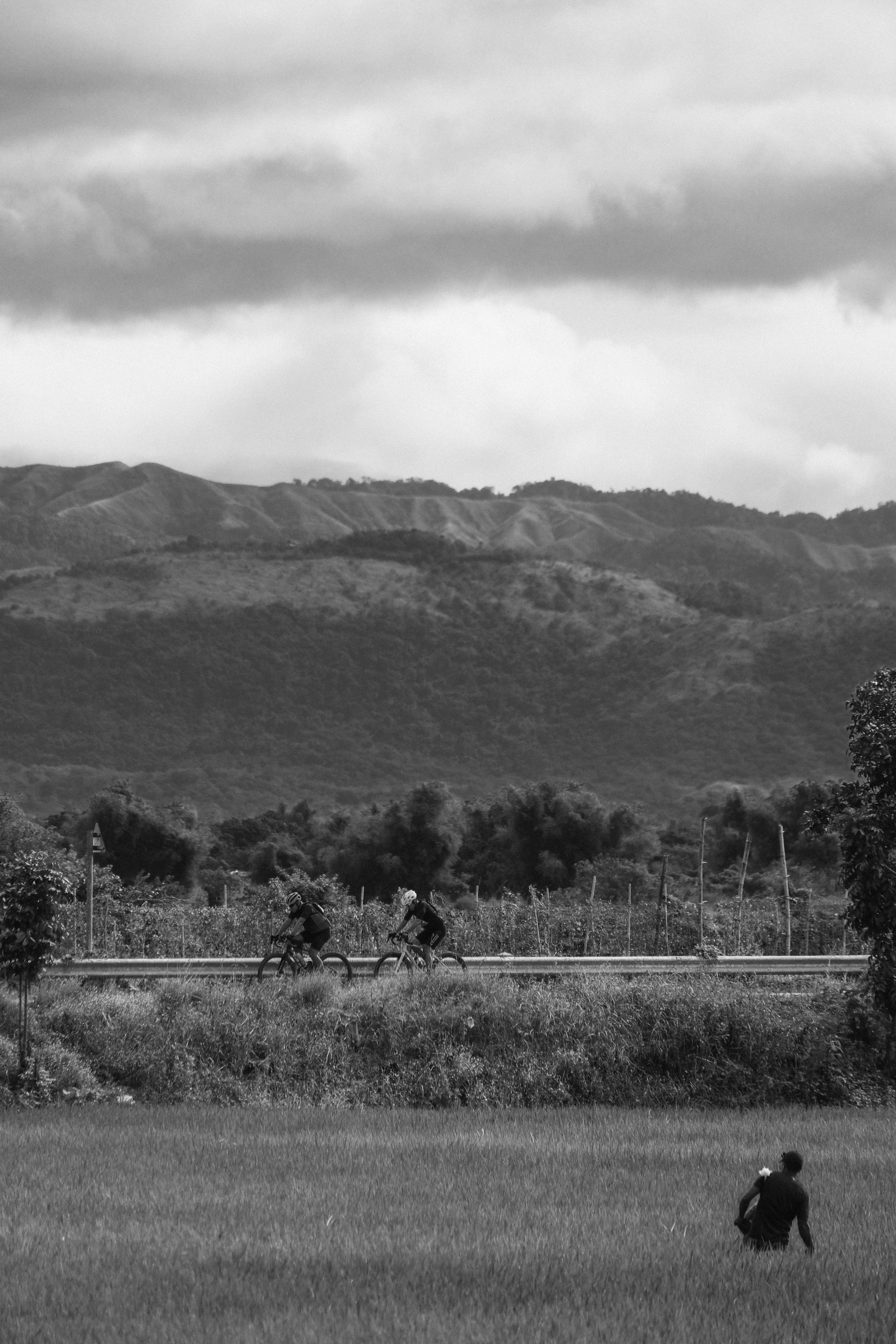 Cyclists riding on rural road through mountainous Philippine countryside in black and white
