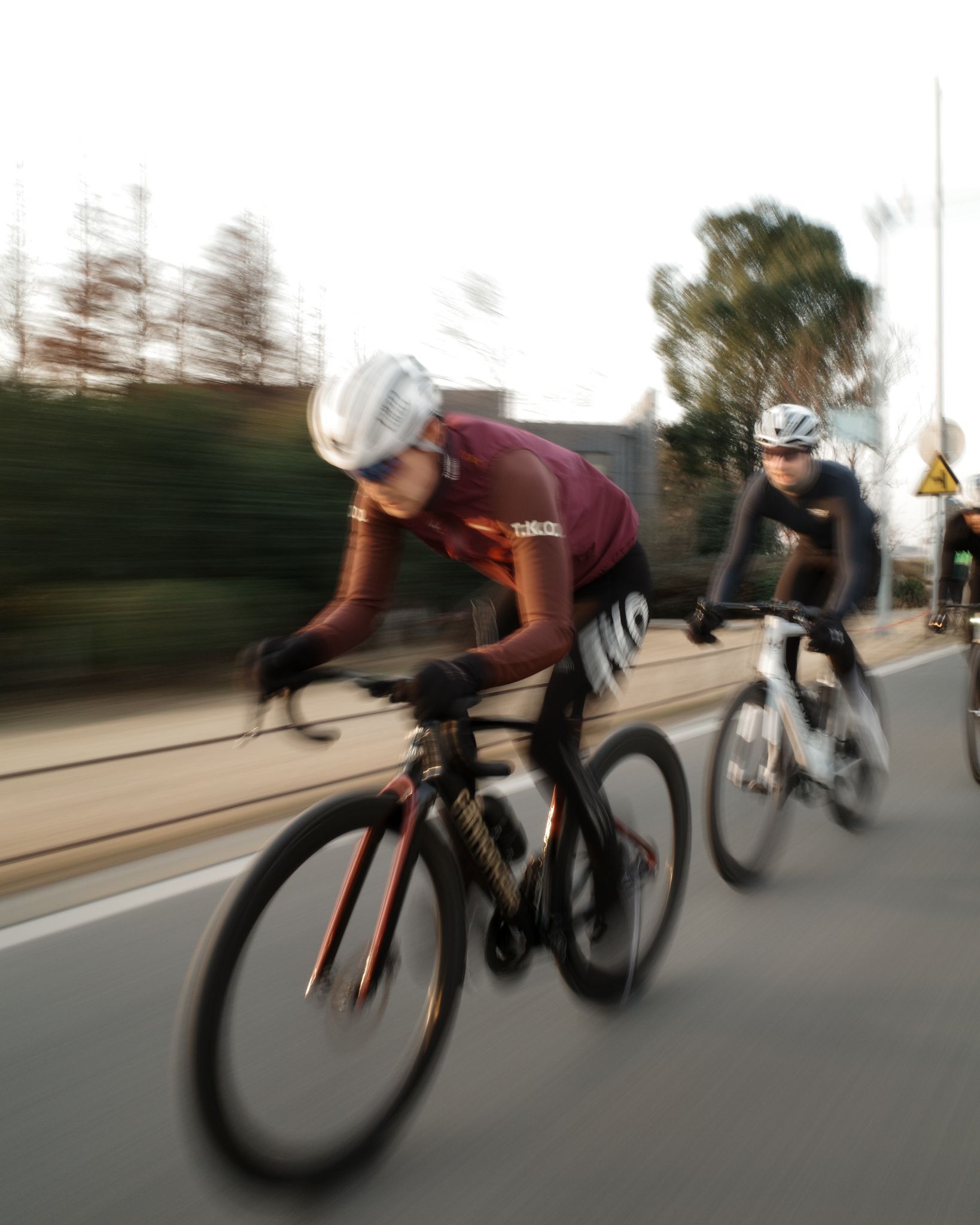 Two cyclists on time trial bikes in motion blur, one wearing burgundy jersey, one in black