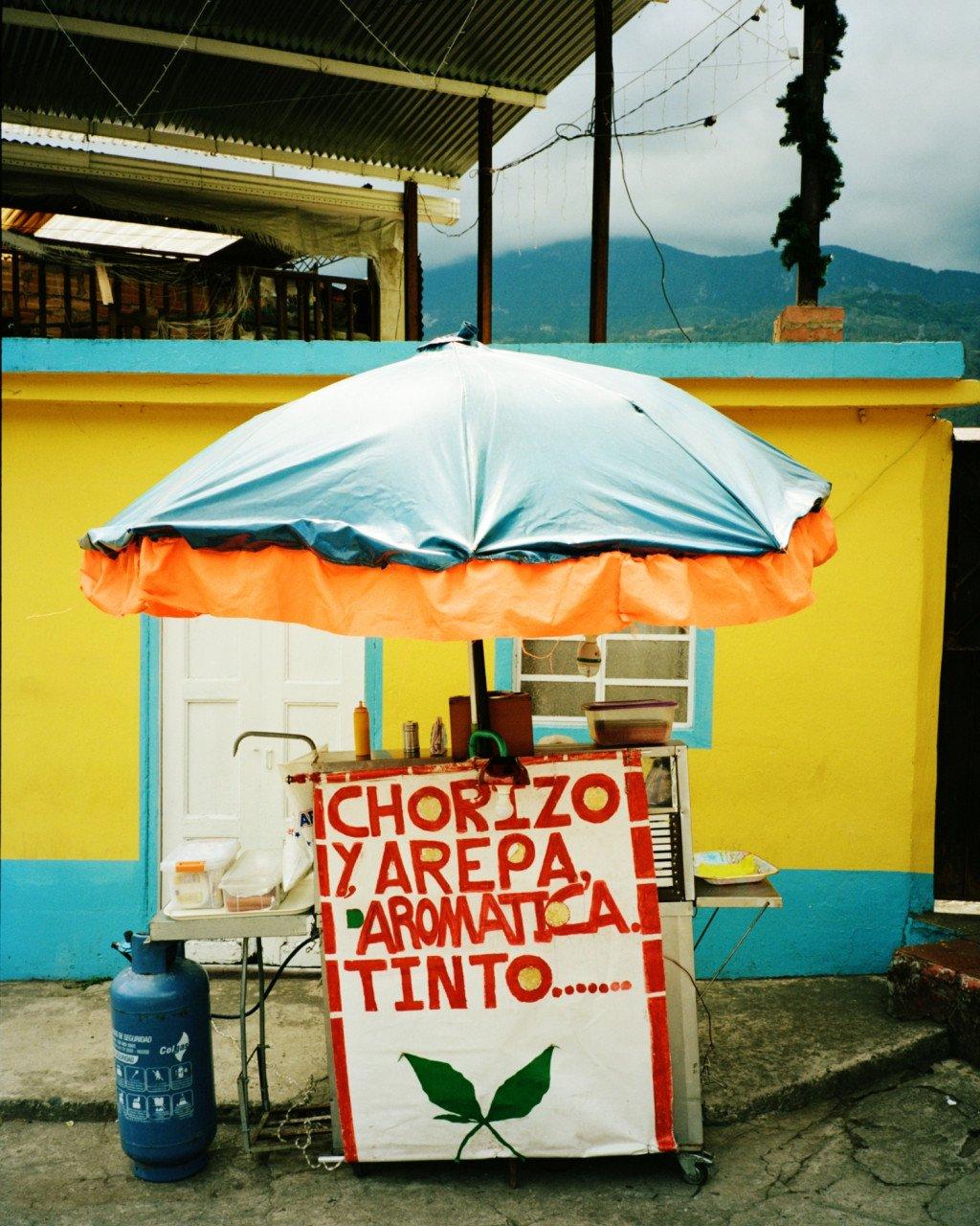 Street food cart with umbrella in front of colorful yellow and blue building in Colombia