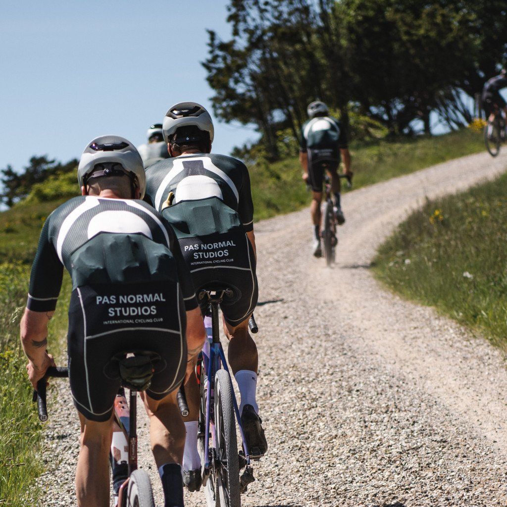 Cyclists wearing black and white racing kits with back branding riding on gravel path