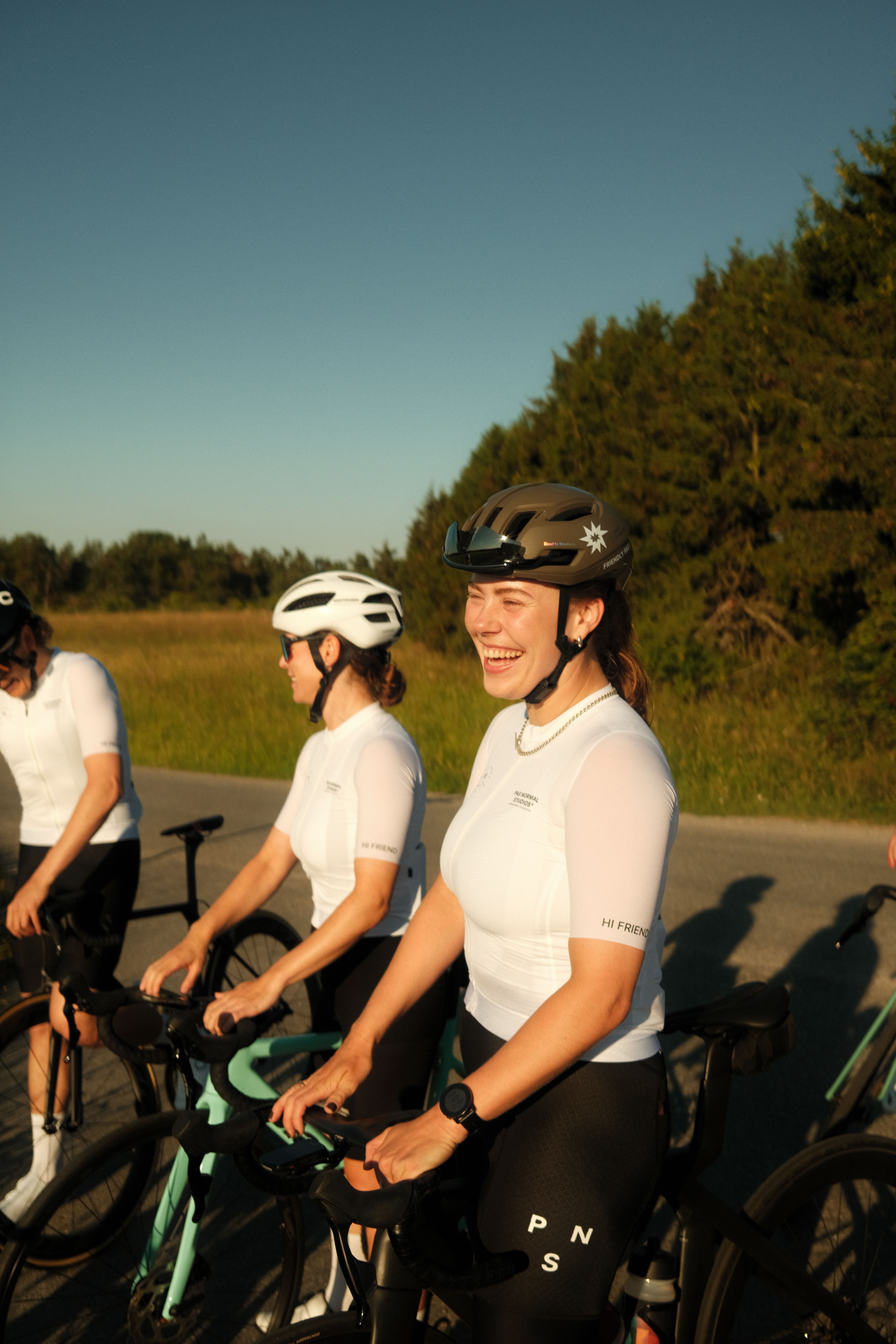 Models wearing white cycling jerseys during group ride on rural road at golden hour