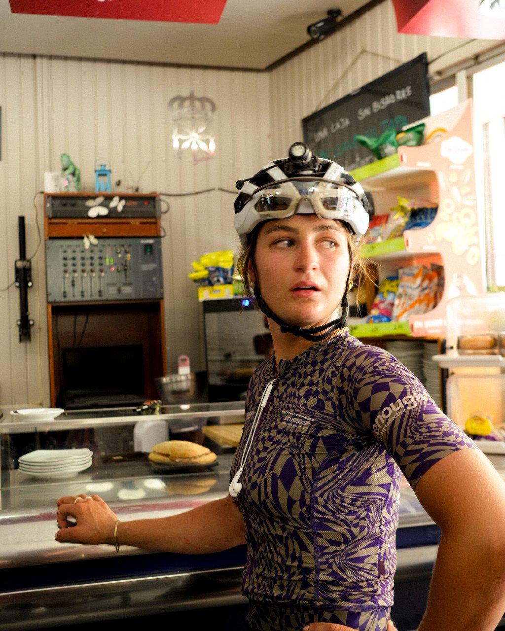 Model wearing purple patterned jersey with white cycling helmet in kitchen setting