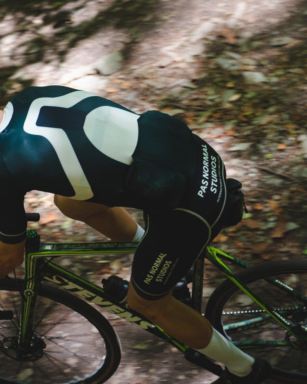 Model wearing black aerodynamic cycling suit with large white graphics in time trial position