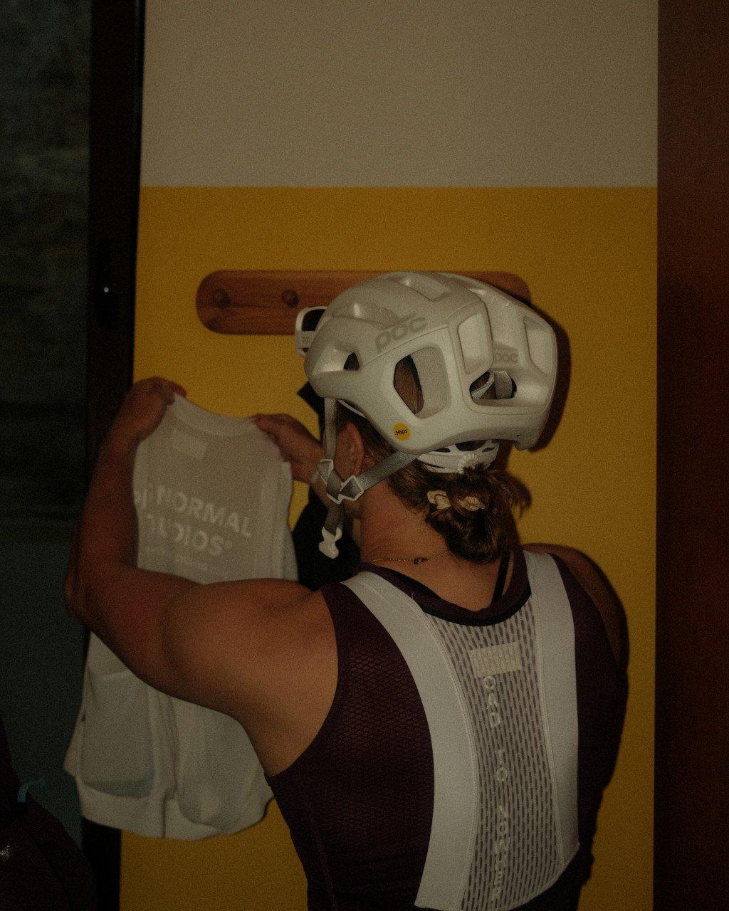 Model wearing white cycling helmet holding grey t-shirt with text in indoor setting
