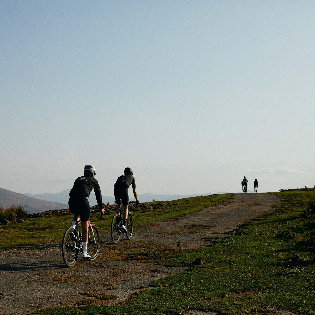 Cyclists on gravel path through green hills with mountains in background