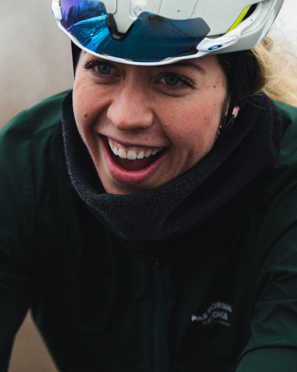 Model wearing dark green winter cycling hoodie with cycling goggles, smiling outdoors