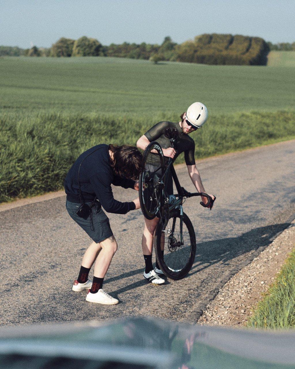 Model wearing black time trial suit with white helmet receiving roadside support in countryside setting