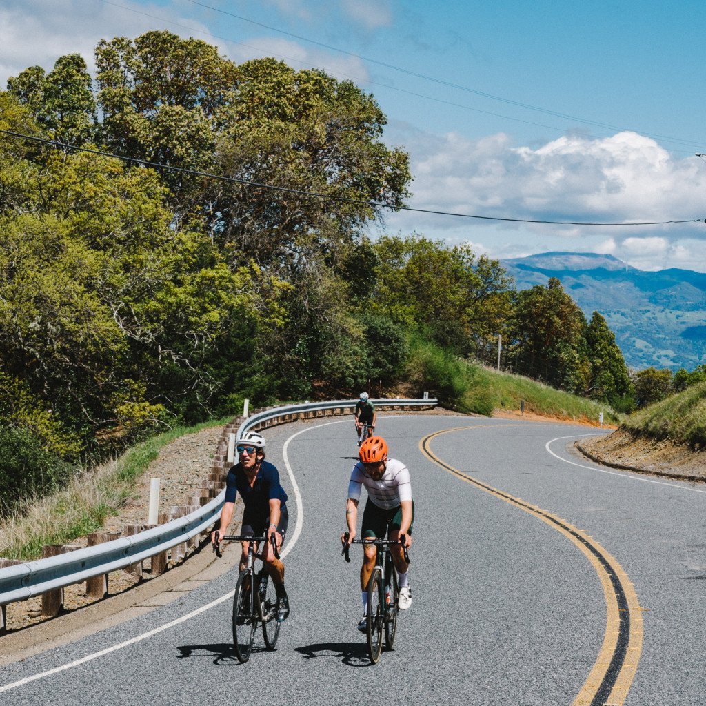 Cyclists riding on winding mountain road with hills and trees in background