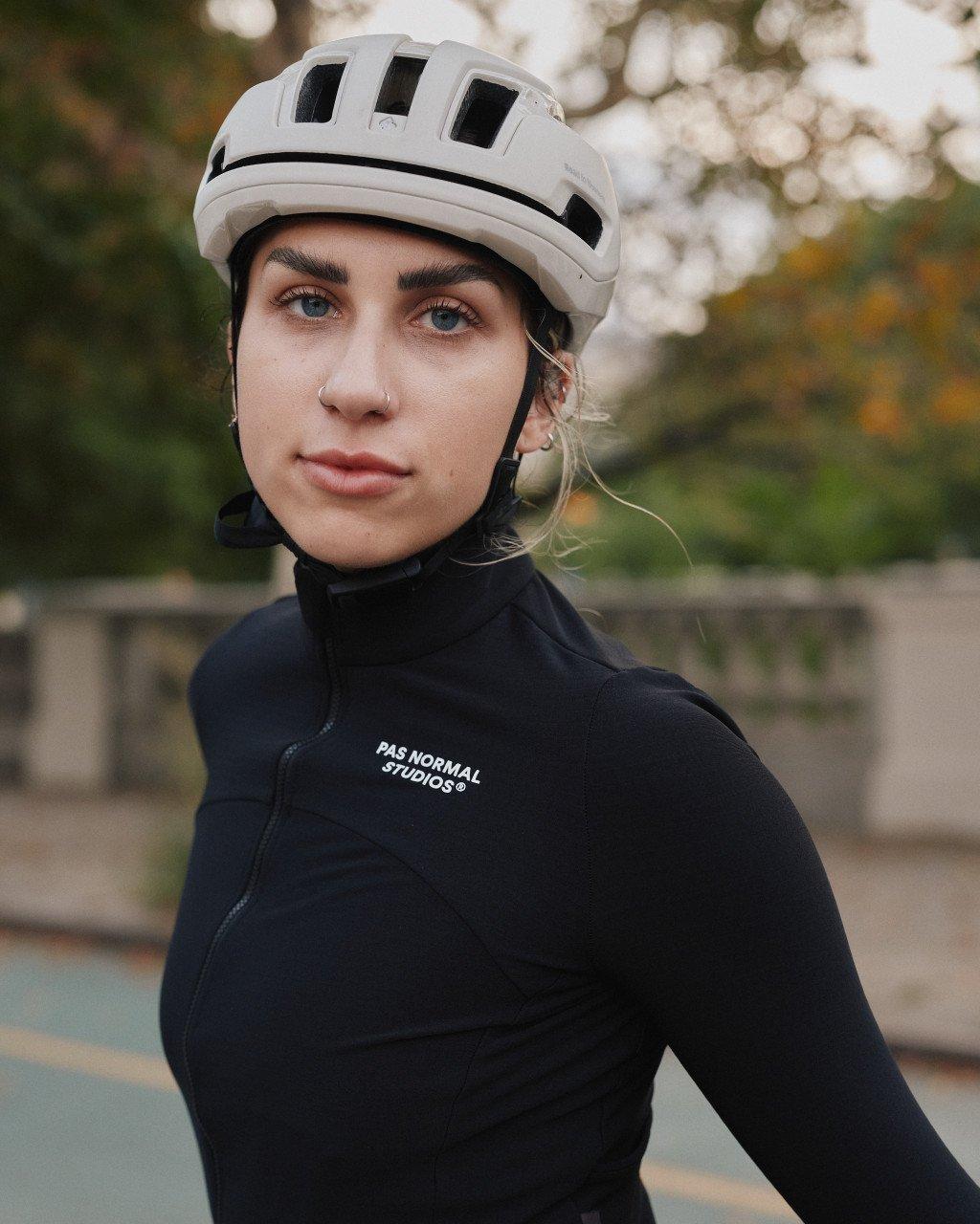 Model wearing black cycling jersey with white helmet and logo branding outdoors
