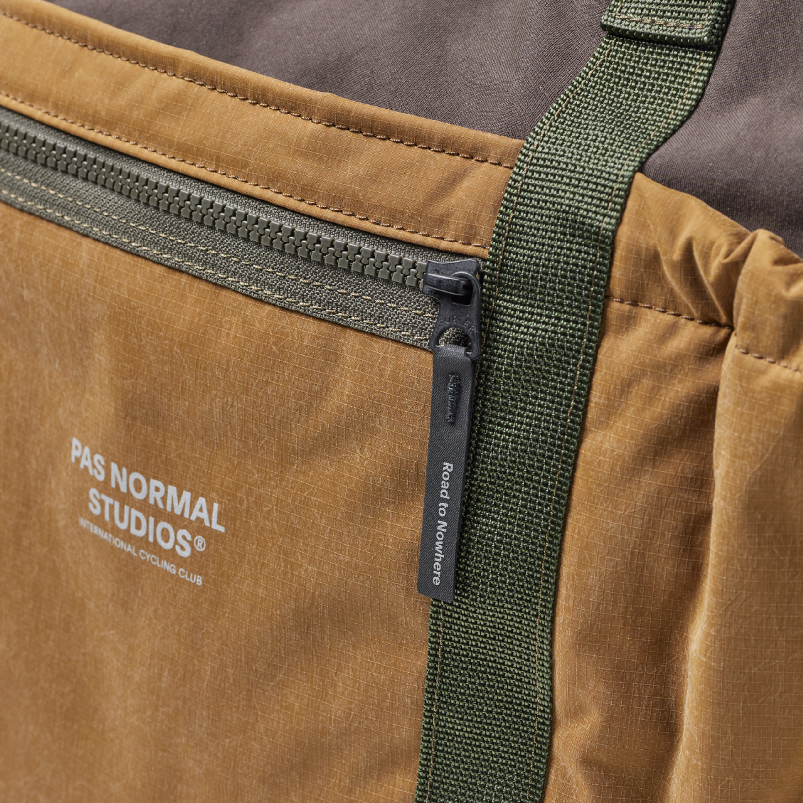Light Brown Porter-Yoshida tote bag, detail view of front zip pocket with green webbing strap and branded zip pull