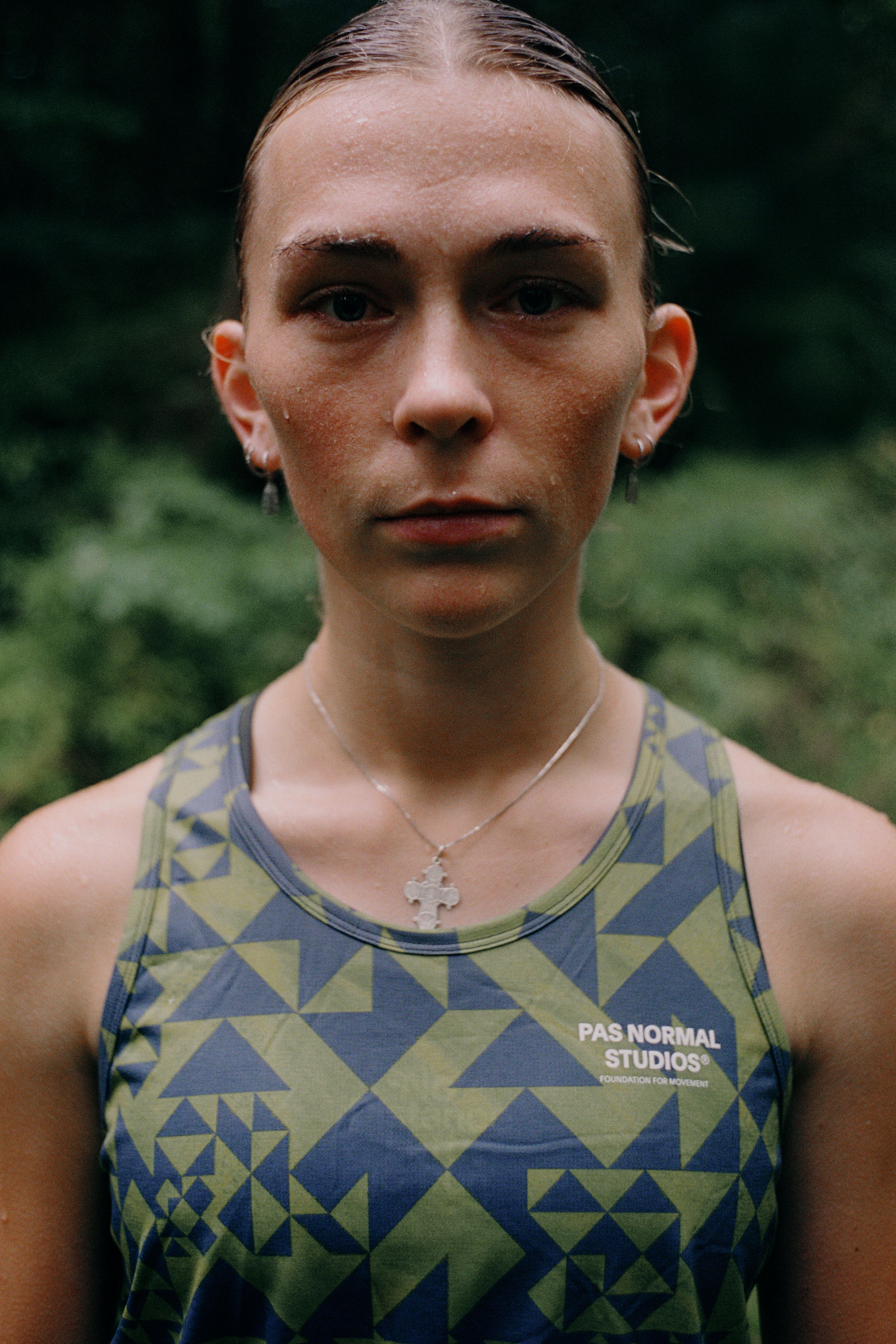Model wearing green and blue geometric patterned cycling tank top with logo, close-up portrait shot