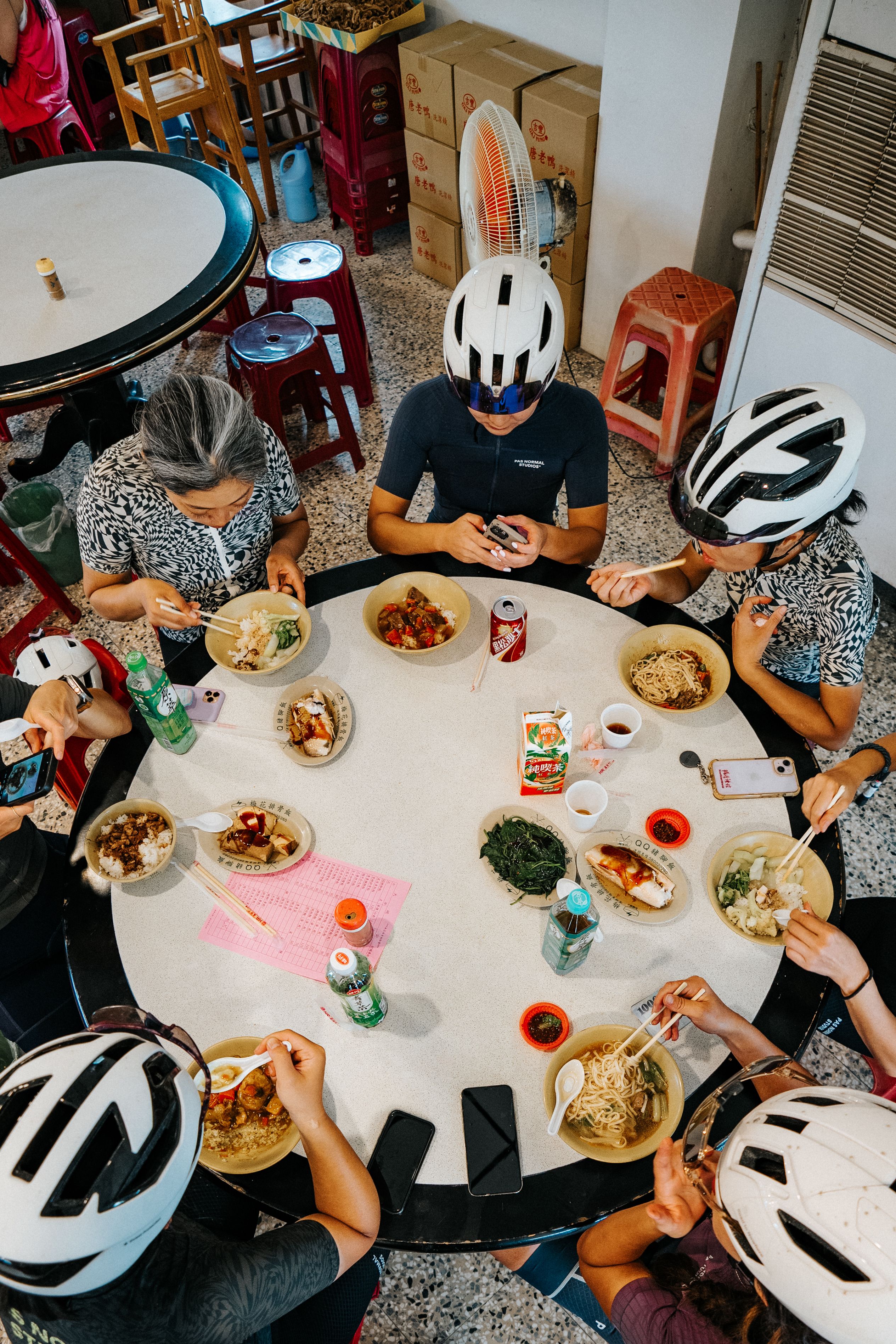 Cyclists in helmets and cycling apparel sharing a meal around table during group ride stop