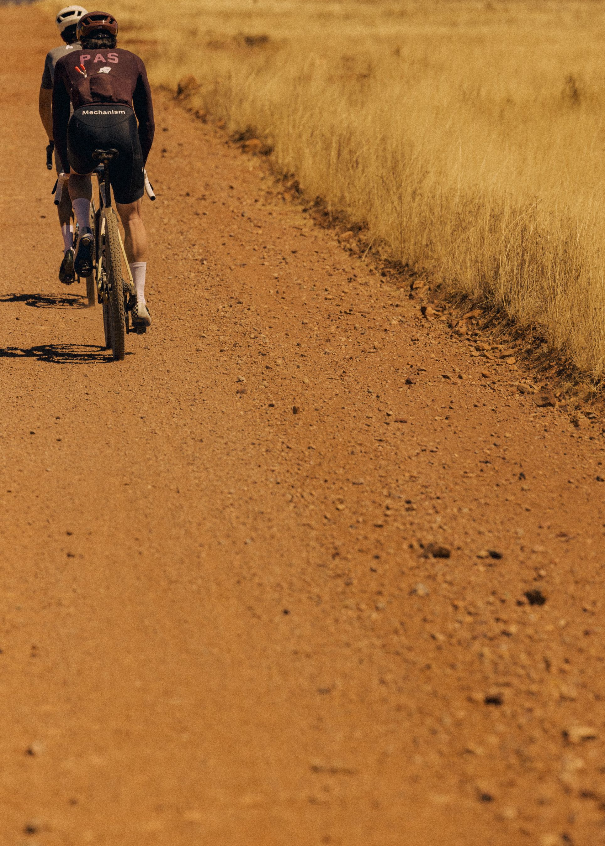 Model wearing Mechanism cycling kit riding dirt road in desert landscape