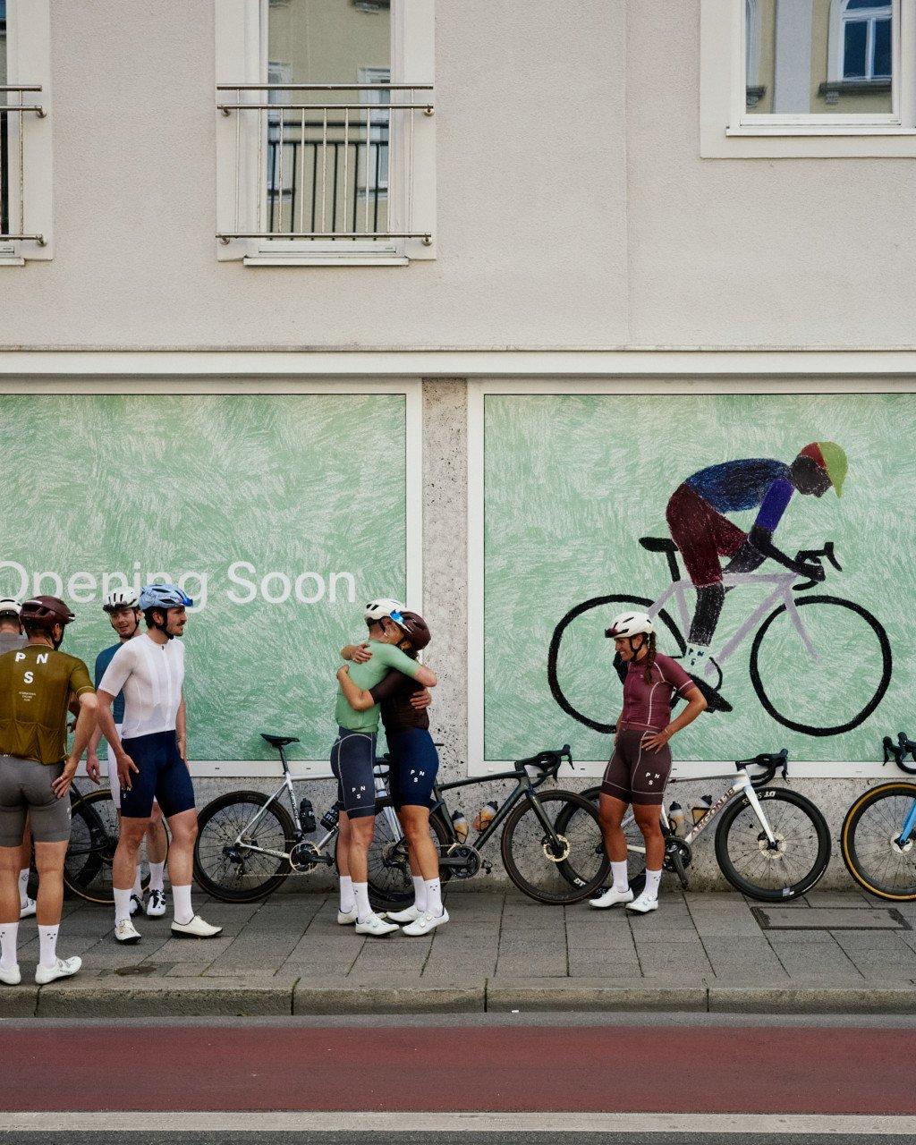 Group of cyclists in cycling apparel standing with bikes outside storefront with green cycling-themed window display