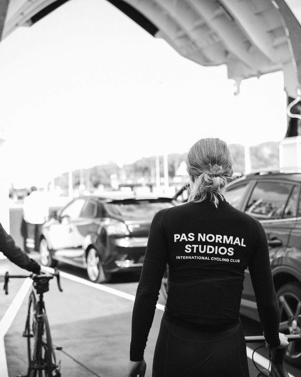 Model wearing black long sleeve jersey with back branding, standing in parking garage with bicycle