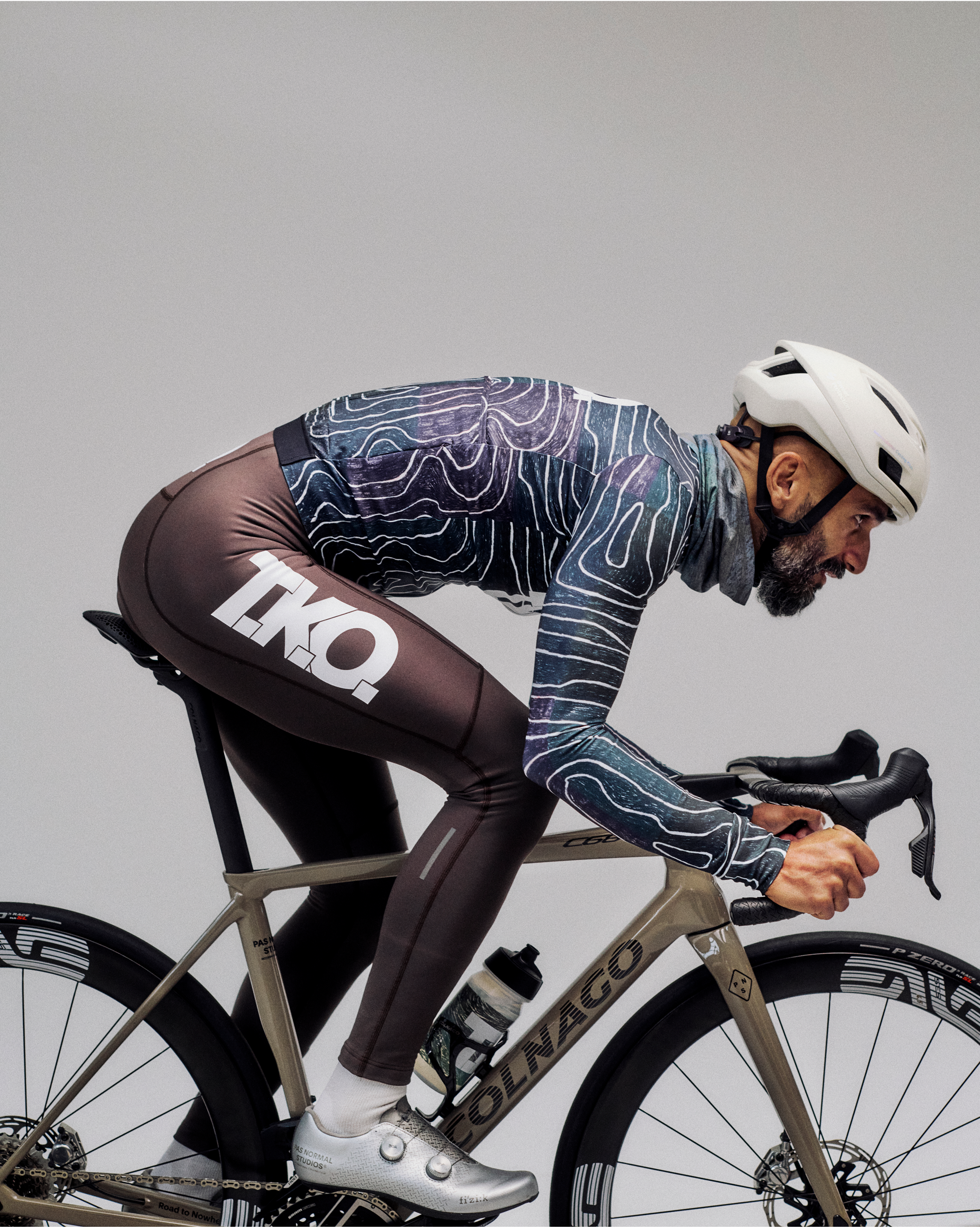 Model wearing men's T.K.O. jersey in blue topographic print with brown bib shorts, aerodynamic cycling position