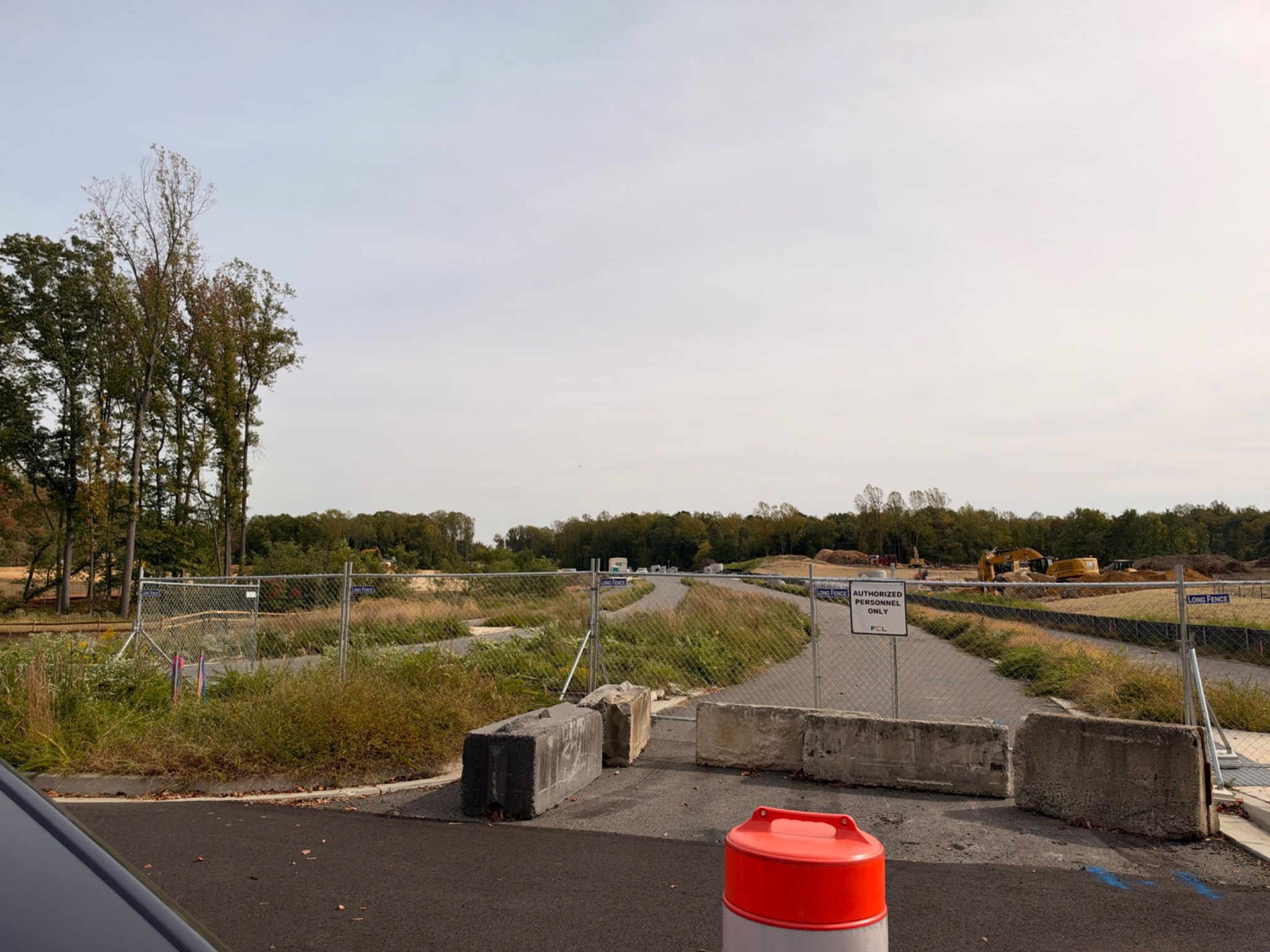 Fencing and concrete barricades close the unopened Presidential Parkway roadway, with cleared land and heavy construction equipment in the distance.