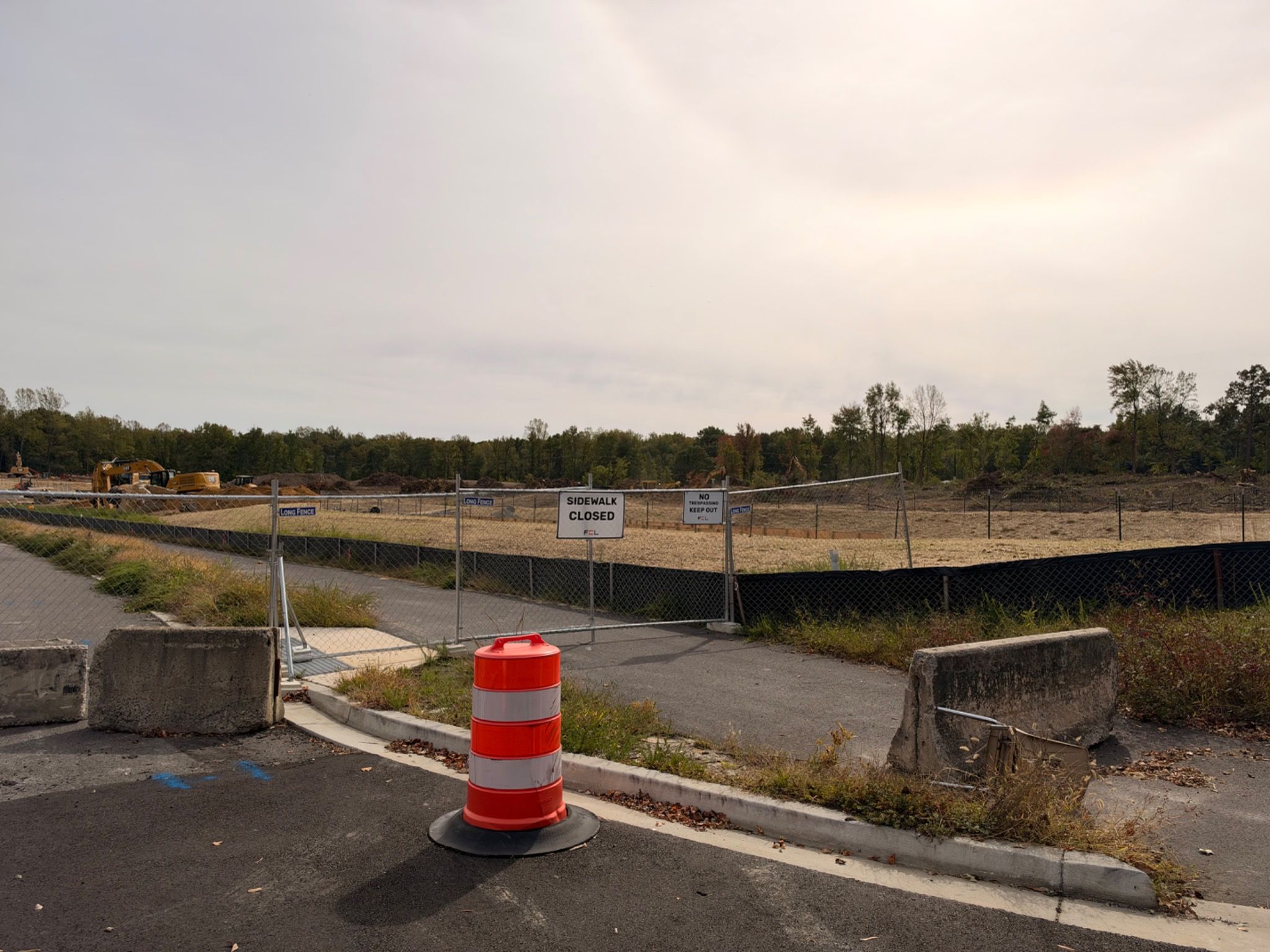 Temporary fencing and concrete barriers block the unopened Presidential Parkway road while clearing and construction equipment appear beyond.