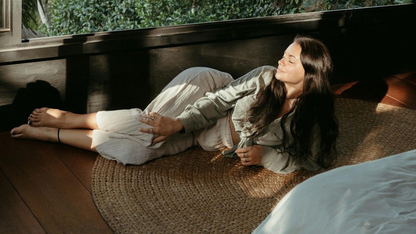 Woman resting on a woven mat beside an open jungle-facing window — Ubud, Bali — OriVista
