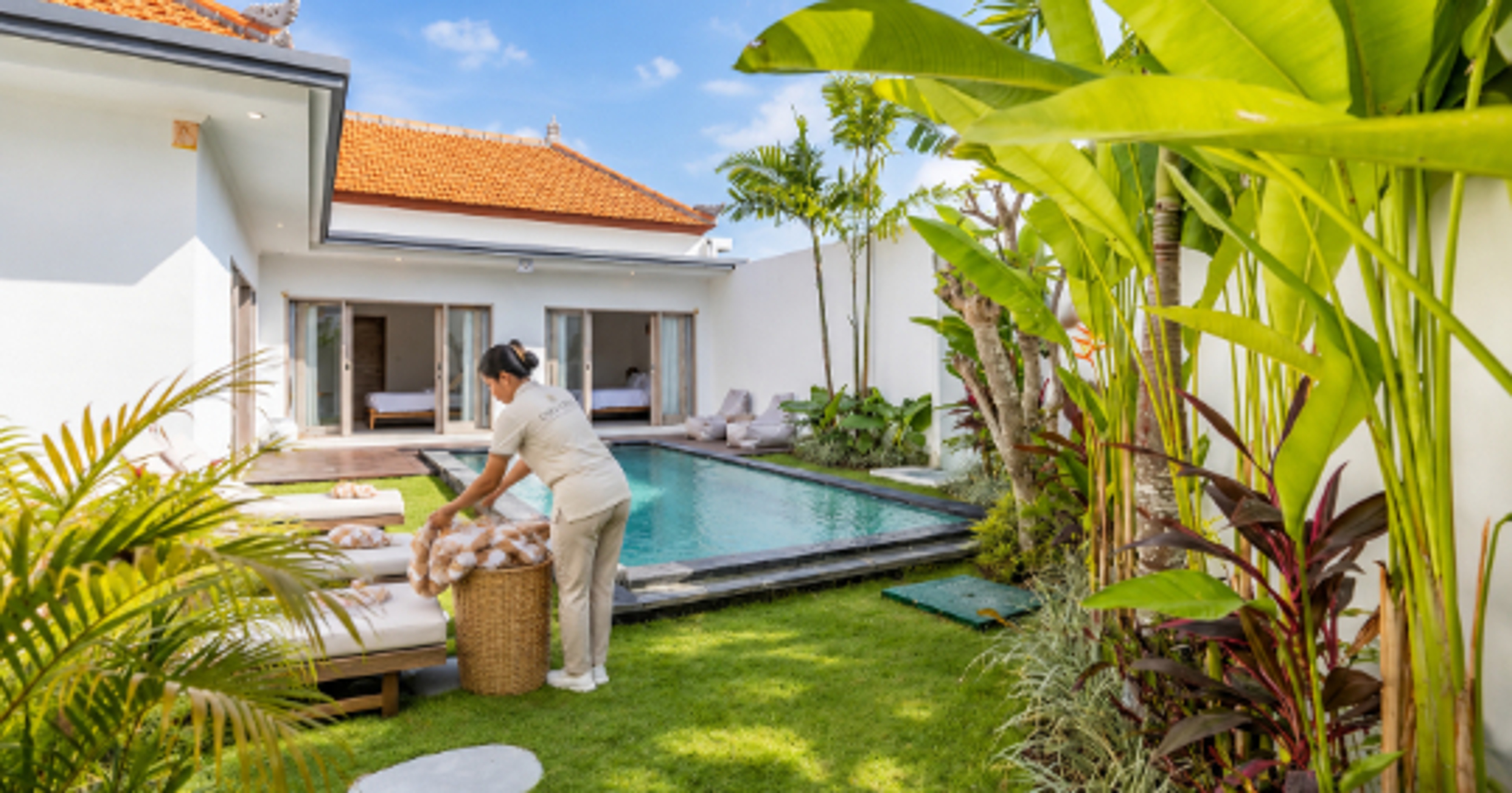 Housekeeper carrying fresh towels across the lawn beside a private pool in a Bali villa