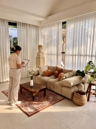 Villa manager in uniform checking a clipboard in a bright Bali villa living room