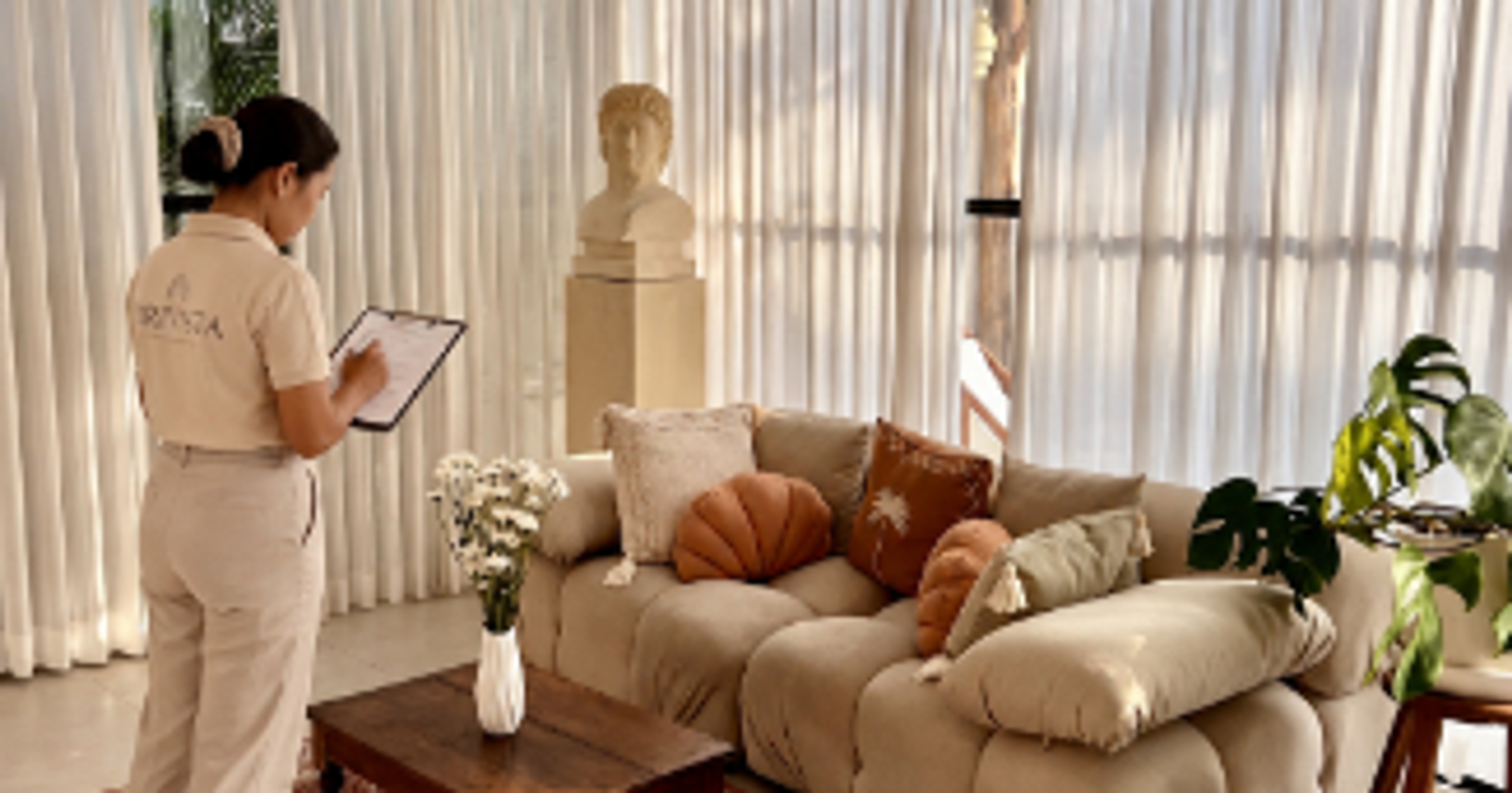 Villa manager in uniform checking a clipboard in a bright Bali villa living room