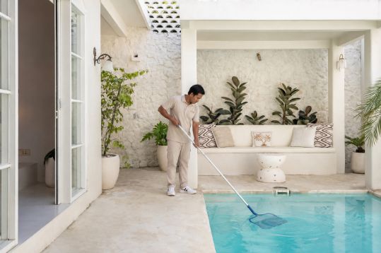 Villa staff member cleaning a private pool in a whitewashed Bali villa courtyard