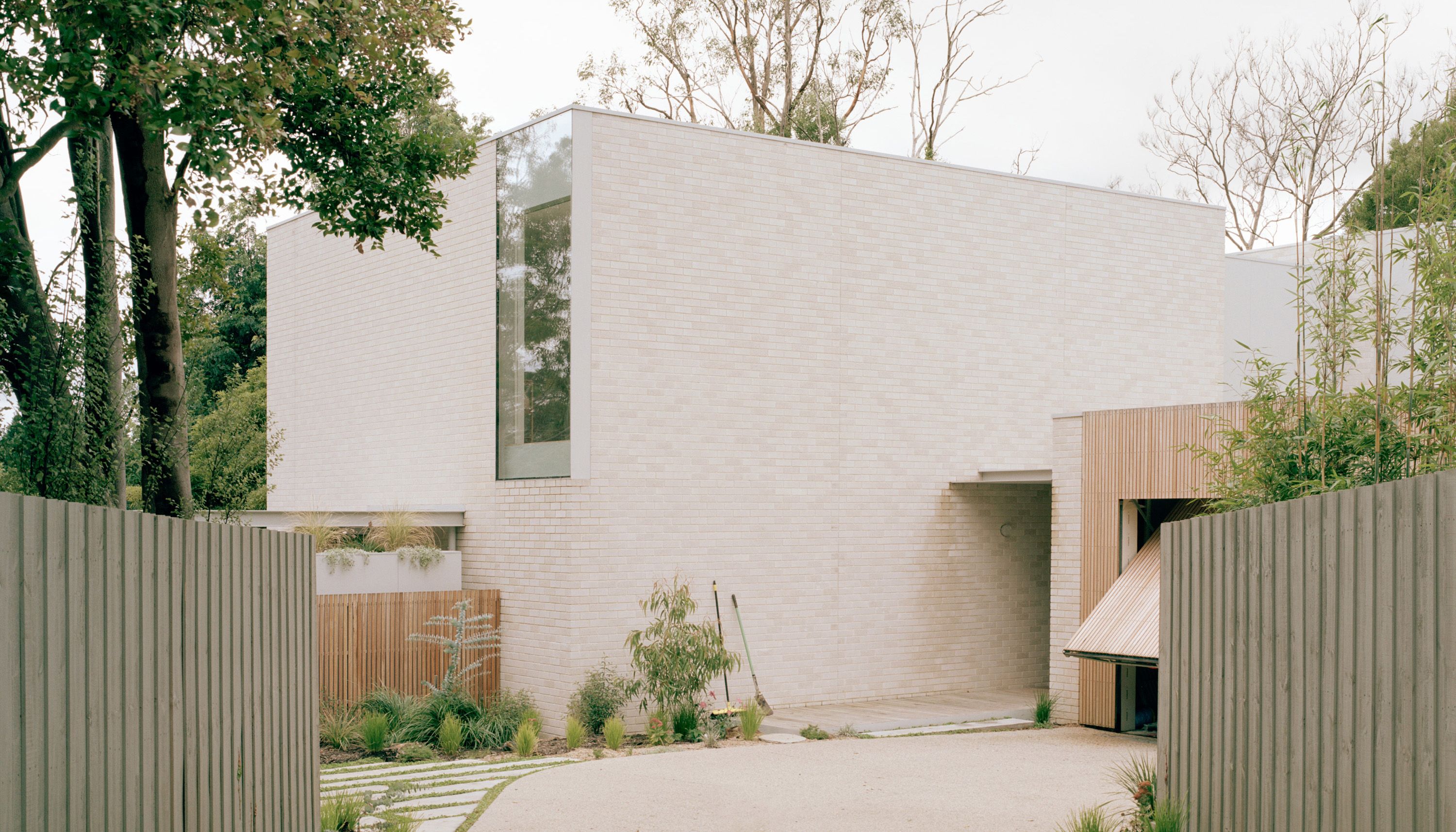 Vasey Pavilions by Jada Homes and Ellul Architecture — pale brick home with timber-clad entrance, set among established trees in Melbourne's outer east