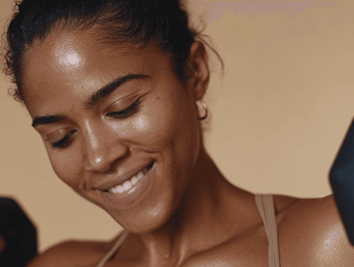 A close-up of a woman smiling and looking down, lit against a warm background